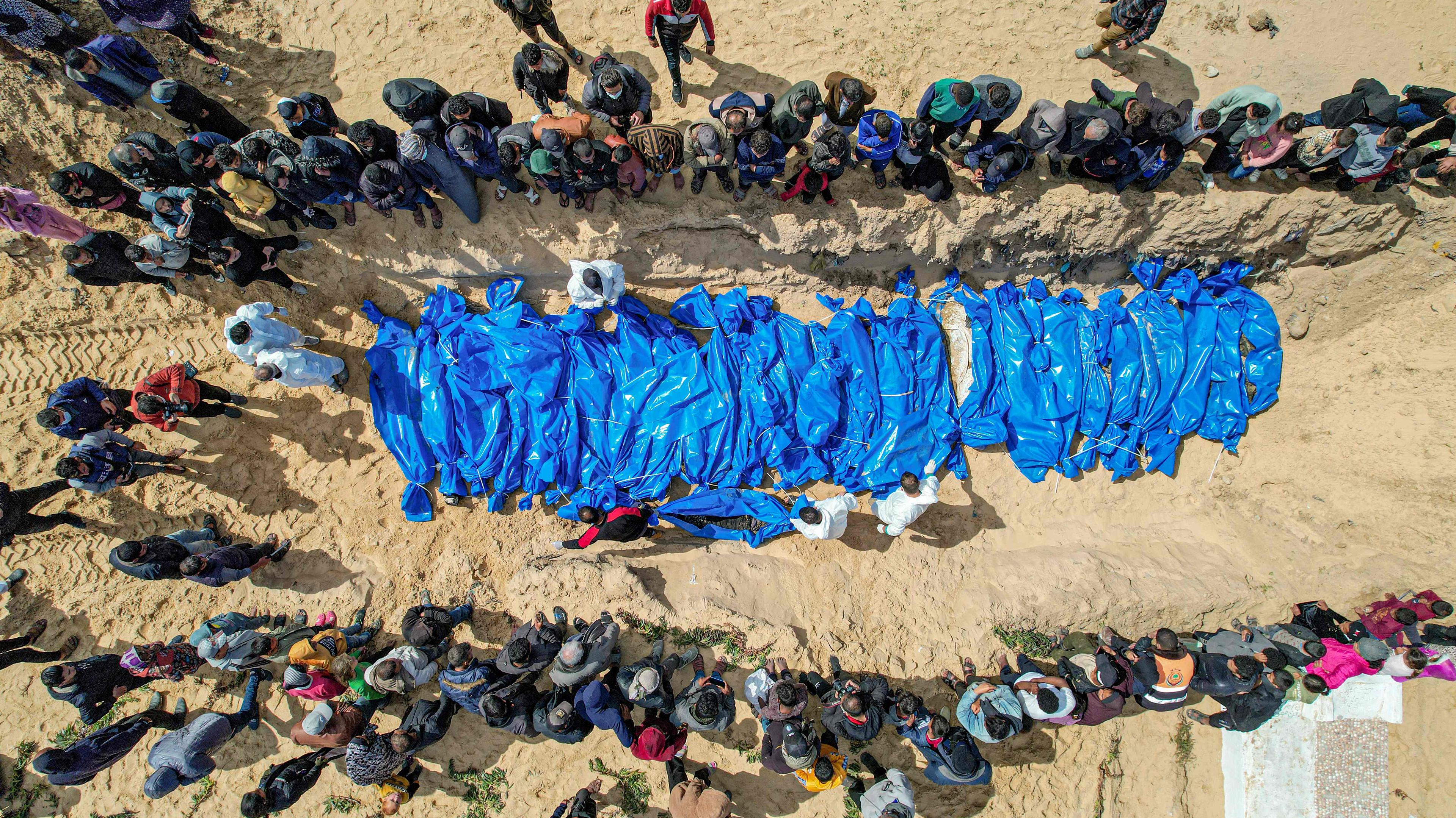 An aerial view shows mourners watching as medical personnel prepare the bodies of 47 Palestinians, that were taken and later released by Israel, during a mass funeral in Rafah in the southern Gaza Strip on March 7, 2024, amid ongoing battles between Israel and the militant group Hamas. 