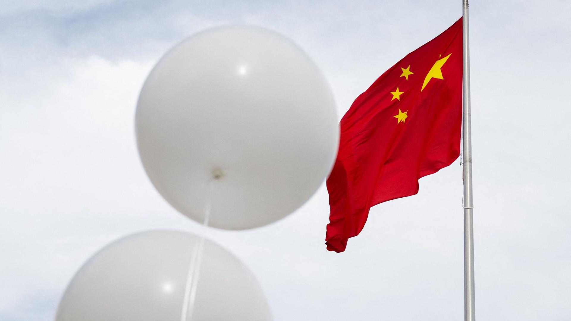 Two white balloons float near the Chinese flag as activist Patrick Mahoney protests against the Chinese government