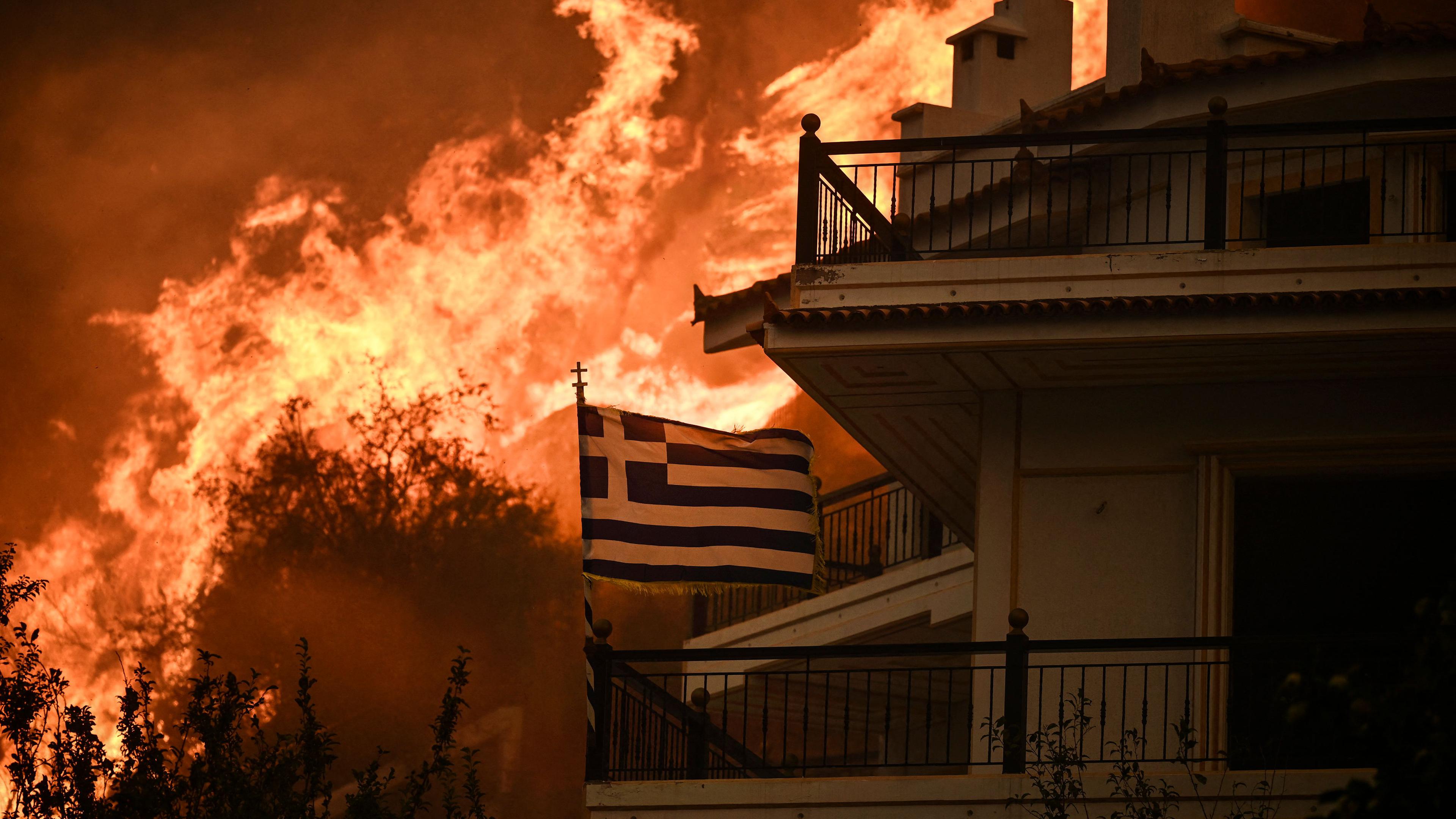 A Greek flag flutters in the wind during a wildfire in Chasia in the outskirts of Athens on August 22, 2023